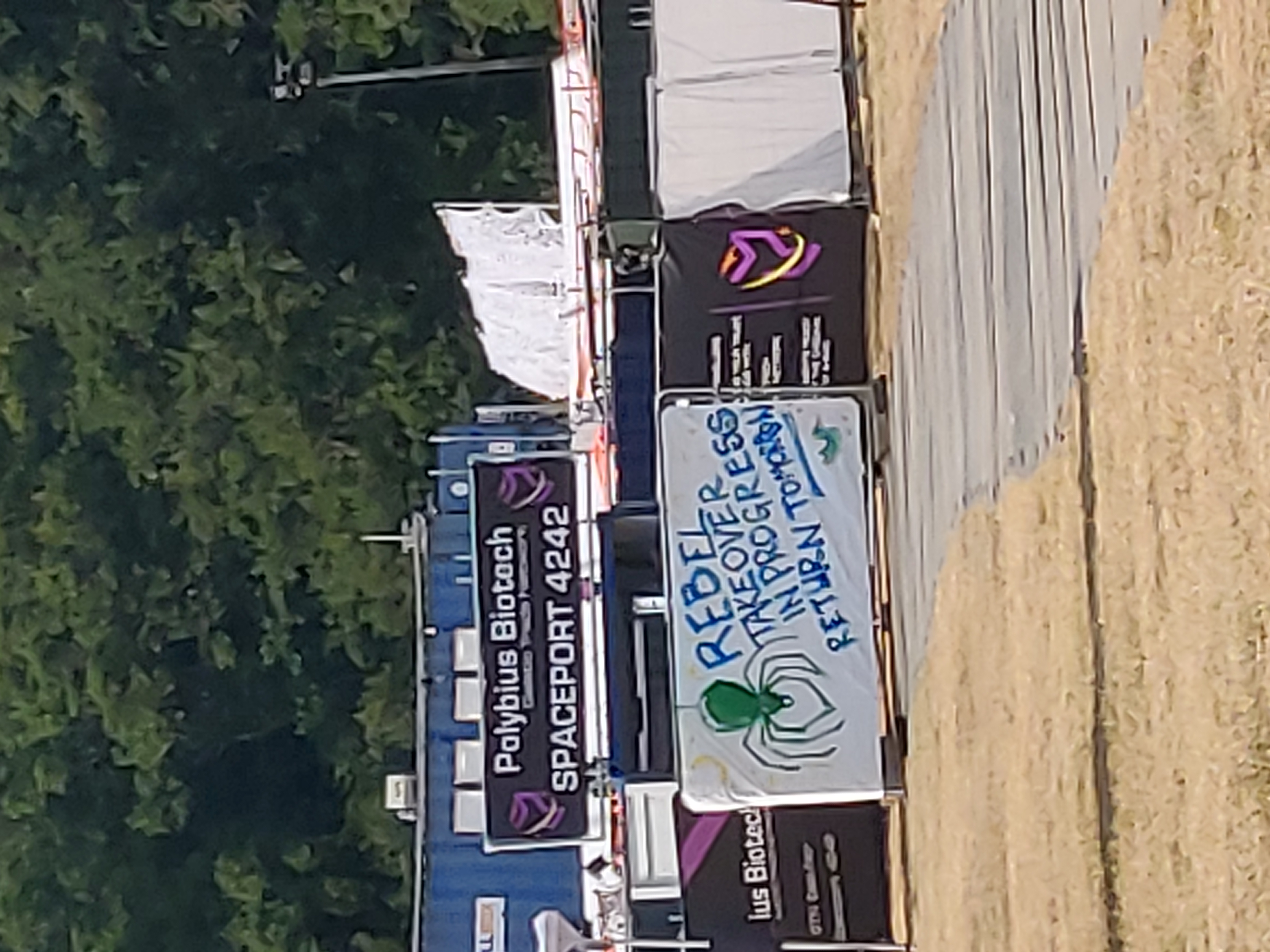 A low quality photo of the entrance to "Polybius Biotech" containers, with a sign saying "Rebel takeover in progress, return tomorrow"